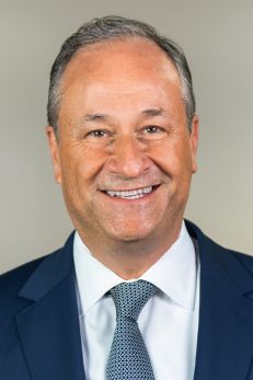 Official portrait of Doug Emhoff, distinguished as the first Second Gentleman of the United States and noted for his Jewish heritage. He is depicted with a welcoming smile, wearing a dark blue suit, white shirt, and a gray patterned tie. The neutral background enhances his professional appearance, emphasizing his role in supporting various societal and community initiatives, and representing an important milestone in American political and cultural history.