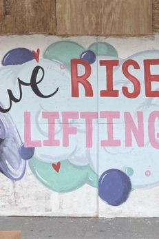 Colorful mural with the text 'We Rise by Lifting Others' promoting community support and empowerment.