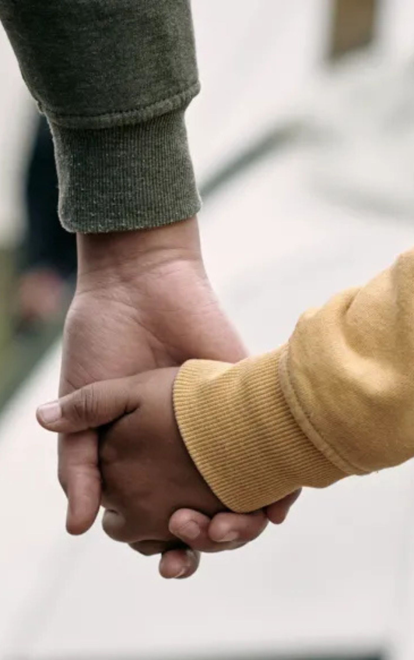 Close-up of two people holding hands, one wearing a green sleeve and the other wearing a yellow sleeve, symbolizing support, care, and connection.