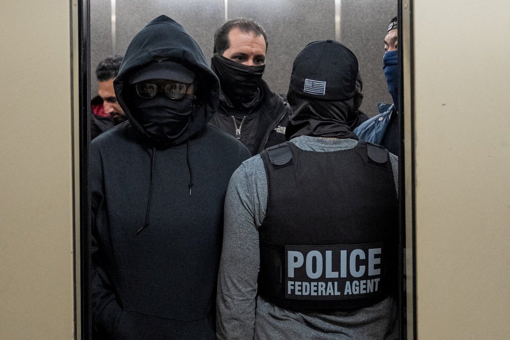 A group of masked individuals stands inside an elevator with a federal immigration officer, whose vest reads “POLICE FEDERAL AGENT.” The scene takes place at U.S. immigration court in Manhattan on November 17, 2025. Photo by David 'Dee' Delgado, Reuters.